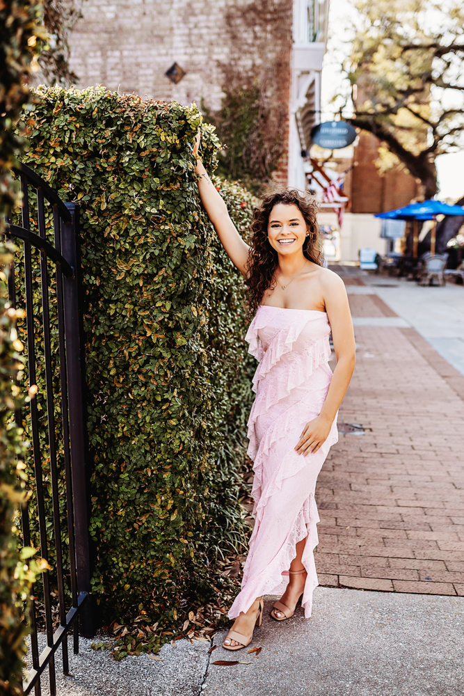 hayden in pink dress leaning on hedges