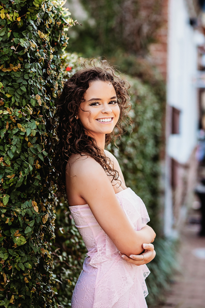 hayden in pink dress leaning on hedges