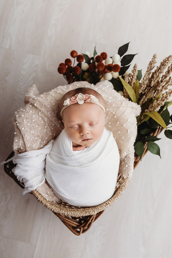 Millie Jo swaddled in a blush wrap nestled in a basket with fall florals at Reflection Images by Tracy Rowell in Florence SC