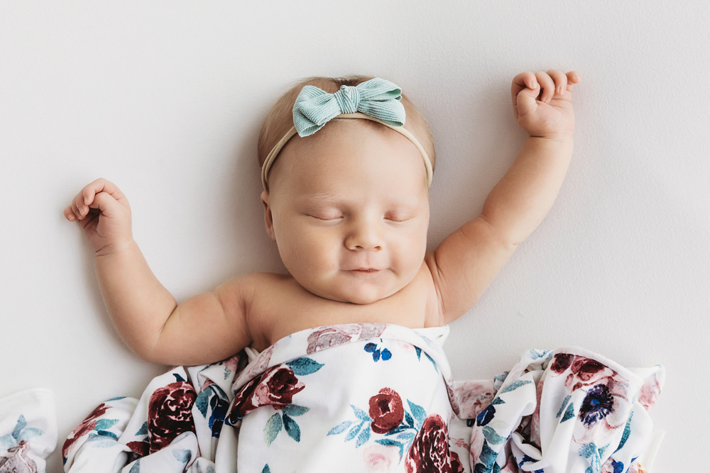 Millie Jo stretching arms in floral blanket with aqua bow on soft white backdrop at Reflection Images by Tracy Rowell in Florence SC