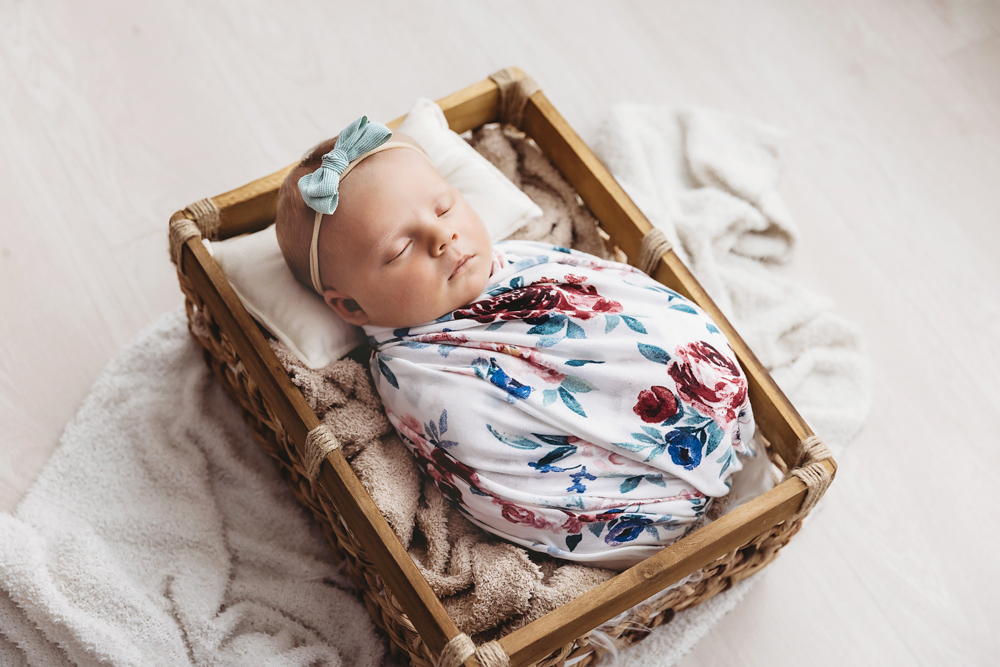 Millie Jo sleeping in wooden box wrapped in floral print with teal bow at Reflection Images by Tracy Rowell in Florence SC