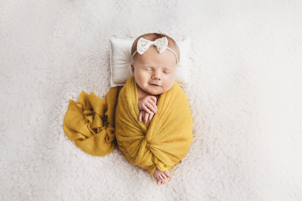 Millie Jo wrapped in mustard yellow on a white flokati blanket at Reflection Images by Tracy Rowell in Florence SC