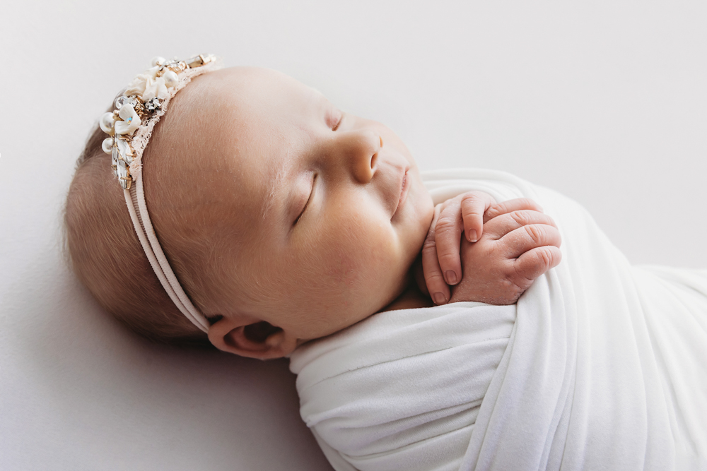 Profile view of Millie Jo resting peacefully in white wrap and pearl headband at Reflection Images by Tracy Rowell in Florence SC