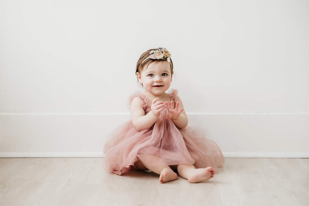 Aubrey in a pink tulle dress and flower headband sitting against a white wall on wood floor at Reflection Images by Tracy Rowell in Florence SC