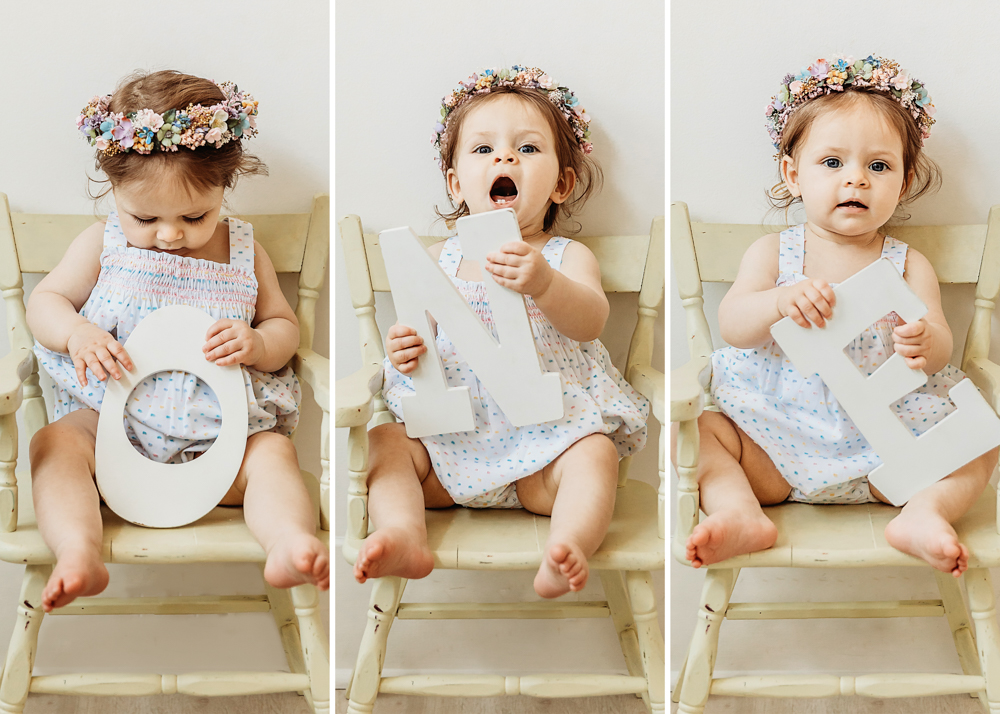 Livi Kate holding O-N-E letters while sitting on a vintage cream chair in a pastel polka dot romper and floral crown at Reflection Images by Tracy Rowell in Florence SC