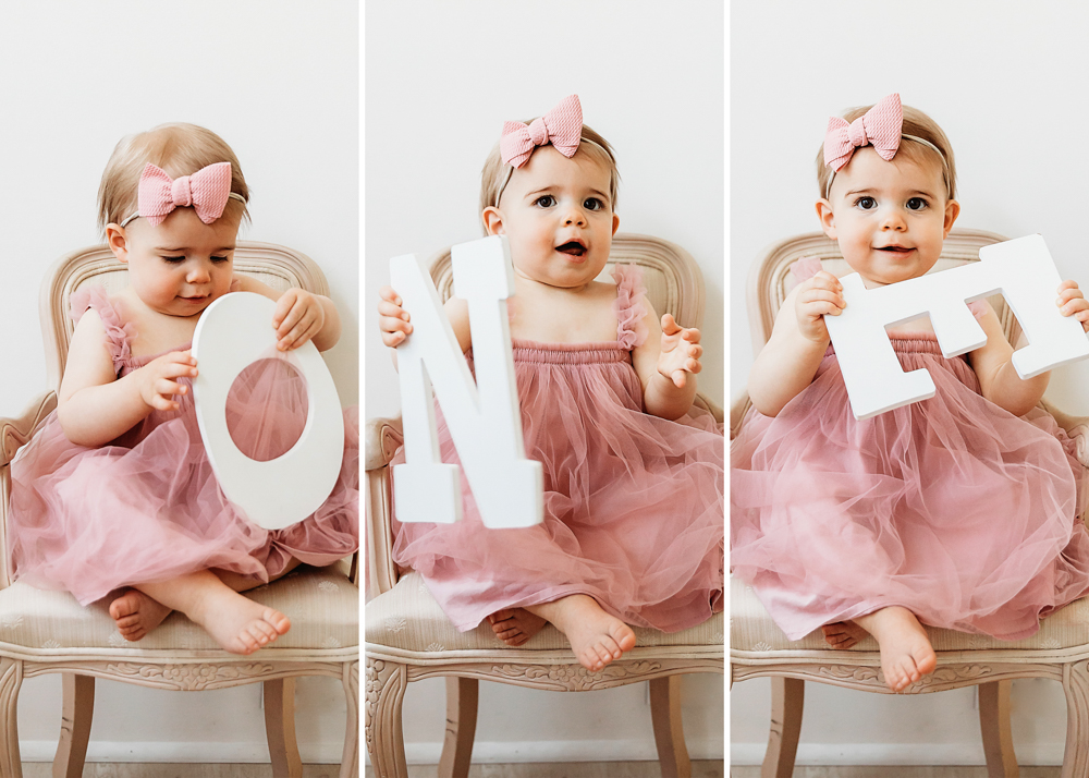 Grace in a pink tulle dress and dotted bow holding O-N-E letters on a vintage chair for her first birthday at Reflection Images by Tracy Rowell in Florence SC