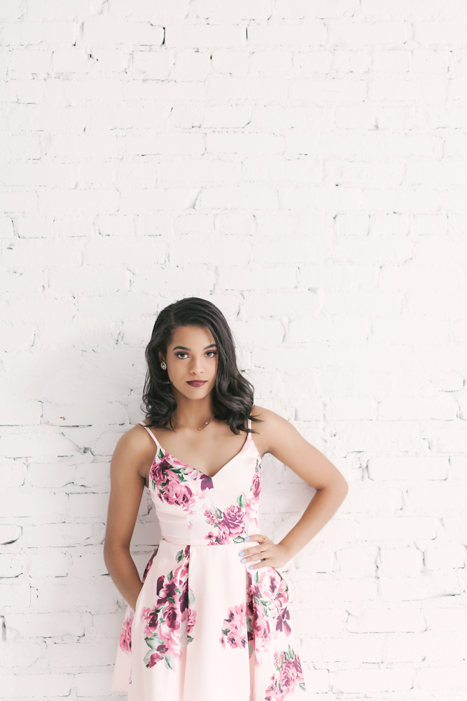 Connie standing confidently in a pink floral dress against a white painted brick wall at Reflection Images by Tracy Rowell in Florence SC