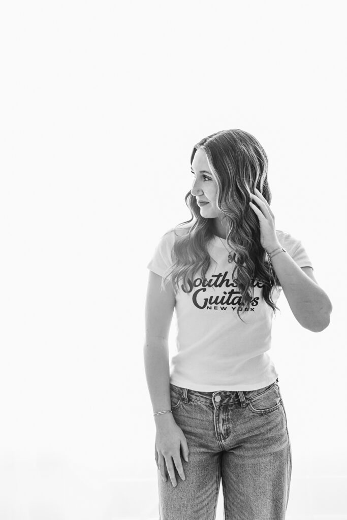 Black and white portrait of Addy softly lit from behind, wearing a graphic tee and jeans, turning slightly in profile at Reflection Images by Tracy Rowell in Florence SC