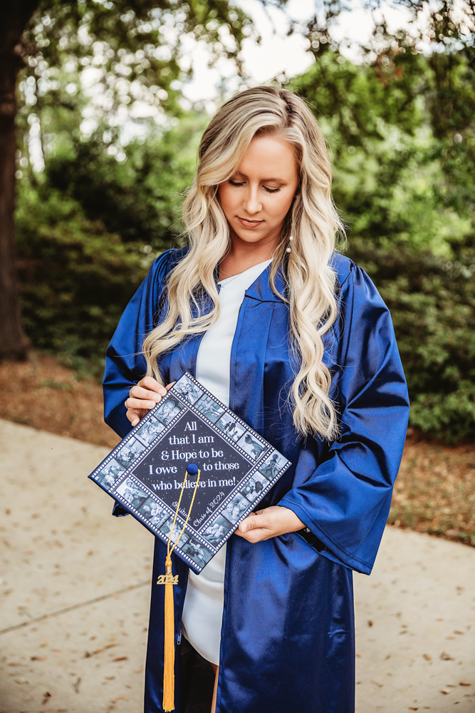Close-up of Kristina looking down at her decorated graduation cap with long curls and soft lighting at Reflection Images by Tracy Rowell in Florence SC