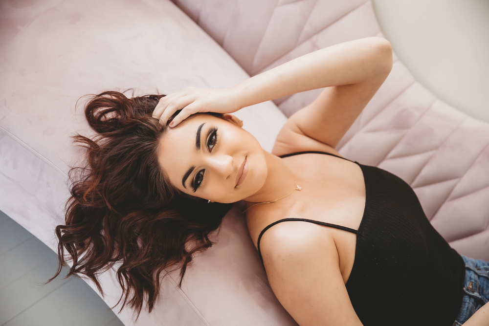 Close-up of Patricia lying on pink sofa with hand in her wavy hair and natural makeup at Reflection Images by Tracy Rowell in Florence SC