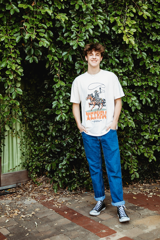 Jack in a western graphic tee and jeans standing relaxed in front of leafy green vines at Reflection Images by Tracy Rowell in Florence SC