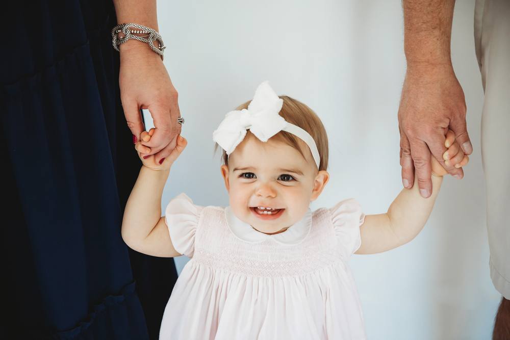 Grace smiling while holding mom and dads hands, framed close-up on her joyful expression and white bow at Reflection Images by Tracy Rowell in Florence SC