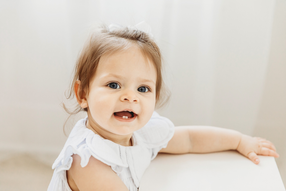 Close-up of birthday girl smiling with soft curls and white bow.