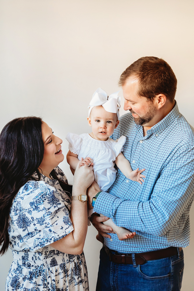 Sweet family moment with Elsie in a white dress and oversized bow, smiling between mom and dad at Reflection Images by Tracy Rowell in Florence SC