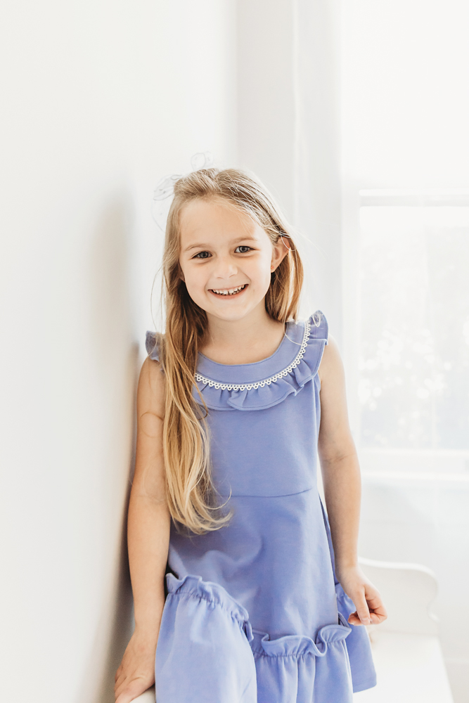 Older sister smiling in natural light wearing a ruffled purple dress.