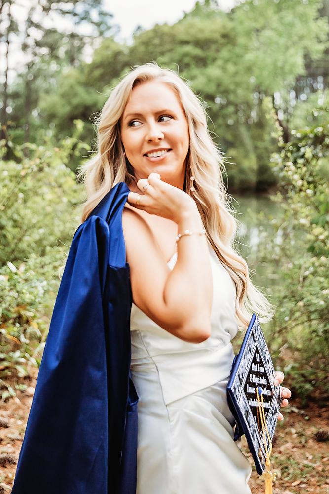 Playful over-shoulder pose of Kristina holding her cap and smiling with natural foliage behind at Reflection Images by Tracy Rowell in Florence SC