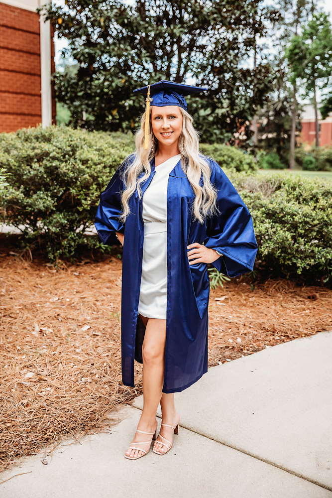 Portrait of Kristina with long blonde curls in a navy gown walking in a wooded setting at Reflection Images by Tracy Rowell in Florence SC