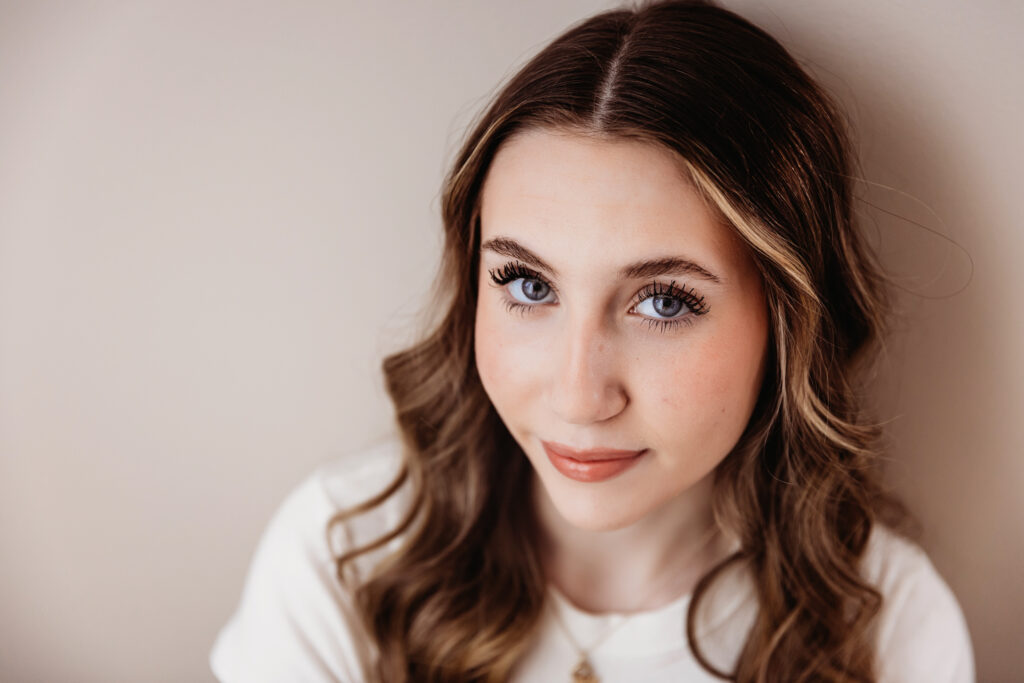 Close-up of Addy smiling softly with clear blue eyes and luminous skin, leaning back against a neutral studio wall at Reflection Images by Tracy Rowell in Florence SC