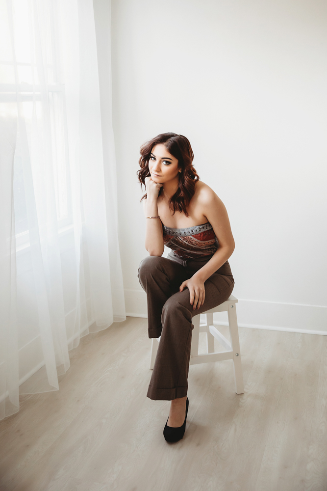 Patricia sitting on white stool in brown pants and strapless patterned top near window at Reflection Images by Tracy Rowell in Florence SC