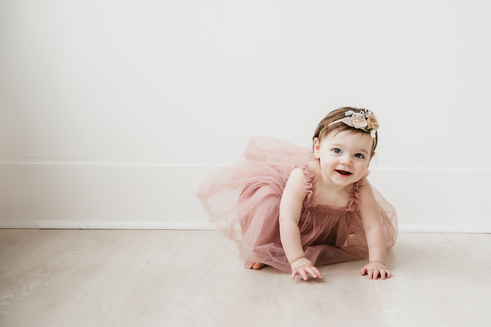 Aubrey crawling playfully on the light wood floor in a pink tulle dress with flower headband at Reflection Images by Tracy Rowell in Florence SC