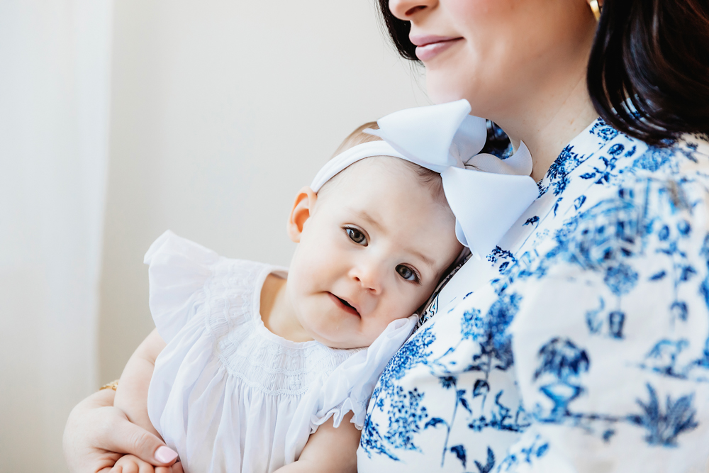 Elsie resting her head on mom’s shoulder, white dress and large bow, natural soft light at Reflection Images by Tracy Rowell in Florence SC