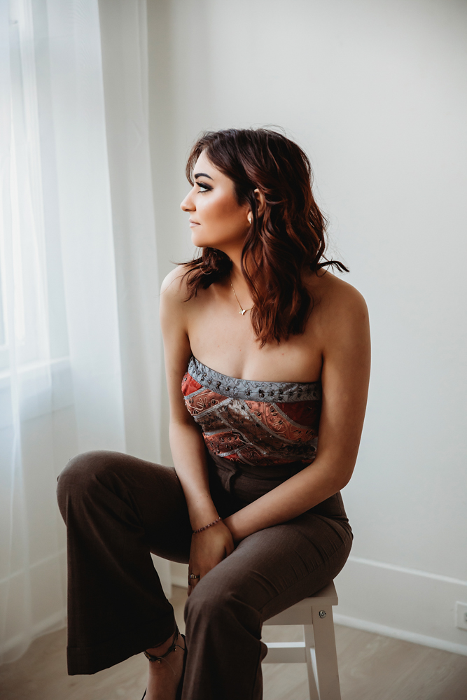 Patricia sitting with chic pose on white stool in stylish brown pants and strapless patterned top at Reflection Images by Tracy Rowell in Florence SC
