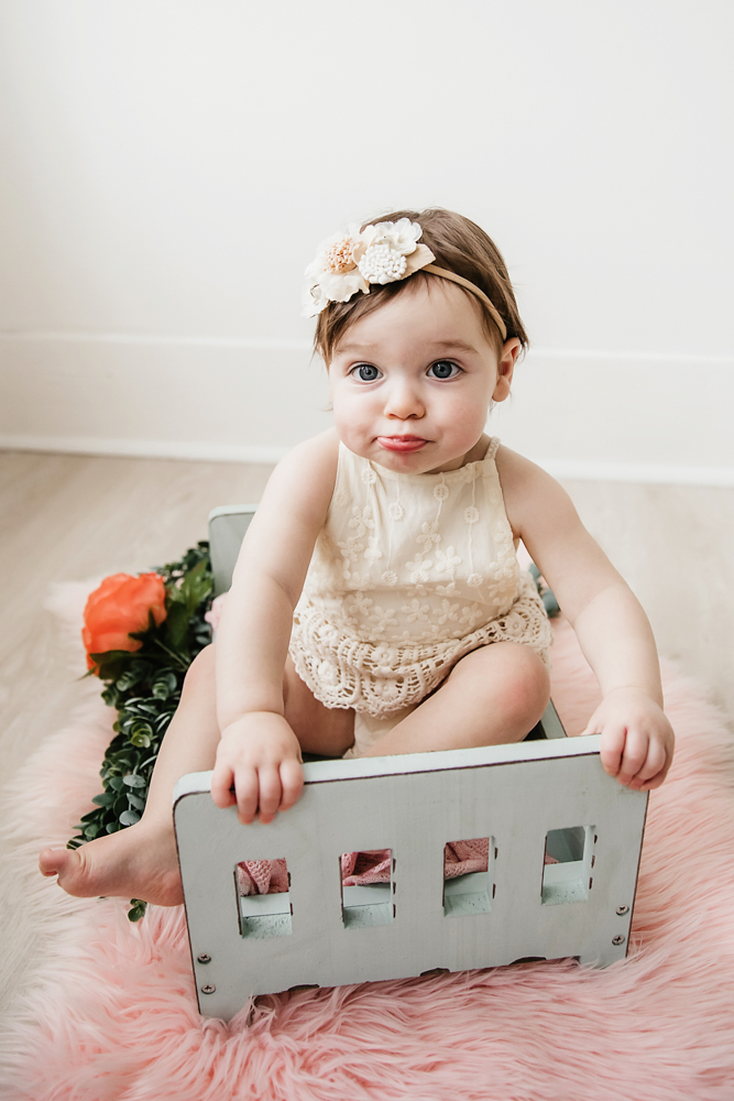 Aubrey seated on a small mint bed with blush and orange flower backdrop, wearing a cream romper at Reflection Images by Tracy Rowell in Florence SC