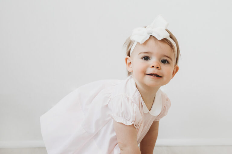 Grace leaning forward with curiosity, wearing a light pink smocked dress and white bow at Reflection Images by Tracy Rowell in Florence SC