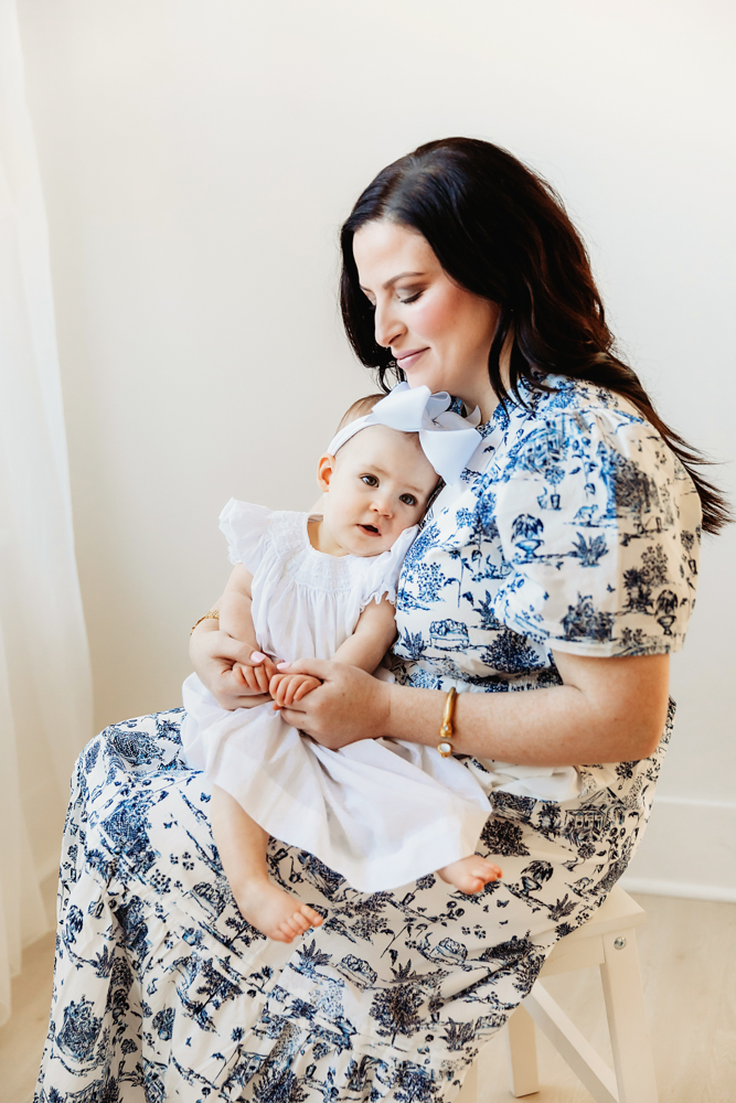 Tender moment with Elsie resting on mom’s lap, white dress and bow, natural light in studio at Reflection Images by Tracy Rowell in Florence SC