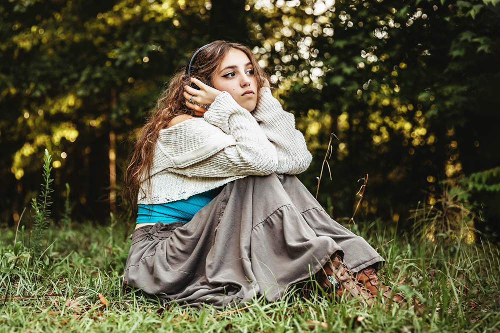 Eve sitting cross-legged in long brown skirt and turquoise top, headphones on, forest backdrop at Reflection Images by Tracy Rowell in Florence SC