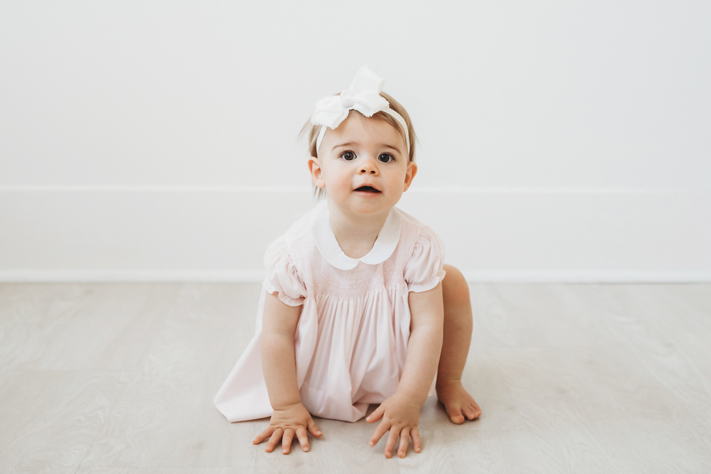 Grace in a white bow and smocked dress sitting with hands on the floor at Reflection Images by Tracy Rowell in Florence SC