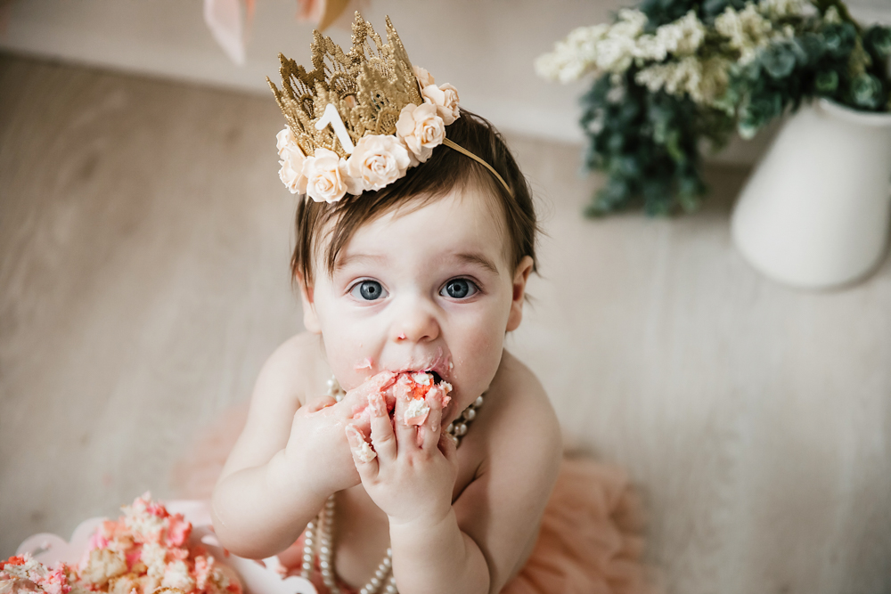 Close-up of Aubrey with cake-covered hands and gold floral crown during her cake smash at Reflection Images by Tracy Rowell in Florence SC