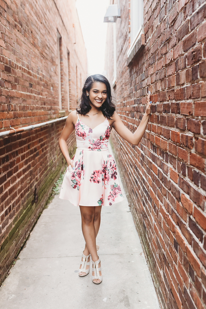 Connie posing in a narrow brick alley downtown with one hand on the wall and a confident smile at Reflection Images by Tracy Rowell in Florence SC