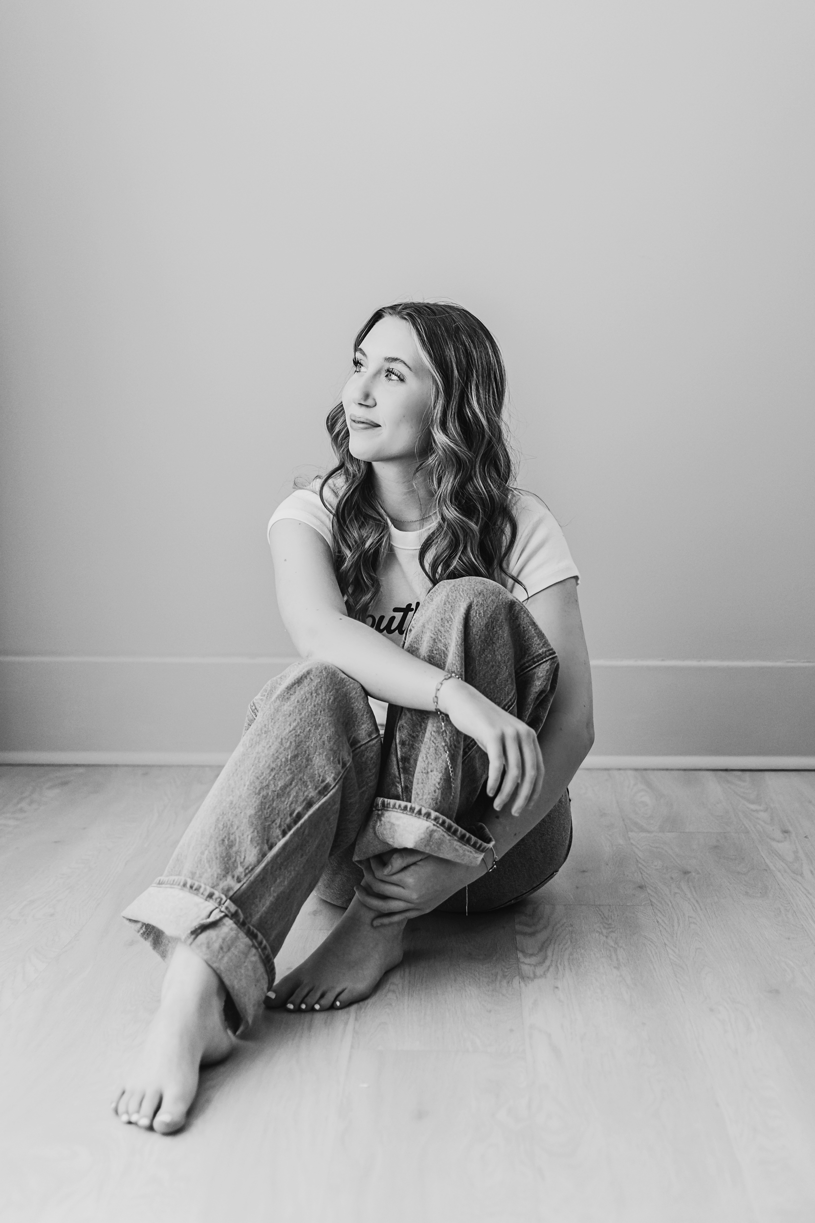 Black and white portrait of Addy sitting on the light wood floor, looking upward with a soft expression at Reflection Images by Tracy Rowell in Florence SC