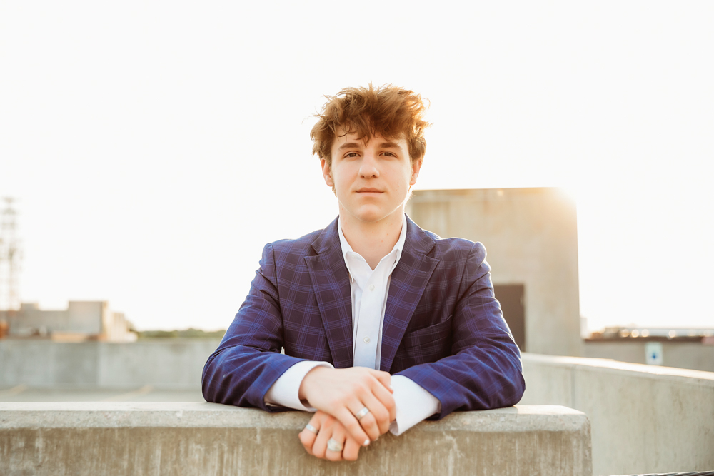 Jack in a blue plaid suit leaning forward with golden sunlight behind him on a downtown Florence rooftop at Reflection Images by Tracy Rowell