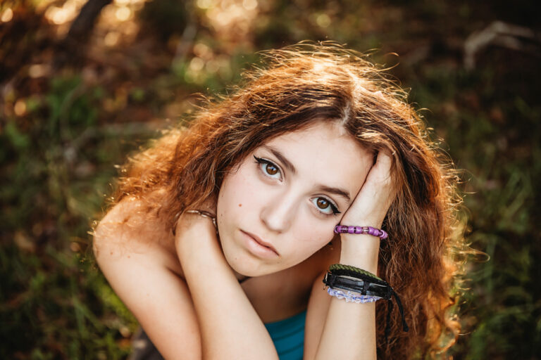 Close-up of Eve resting face in hands, bracelets on wrists, direct gaze with warm sunlight on her hair at Reflection Images by Tracy Rowell in Florence SC