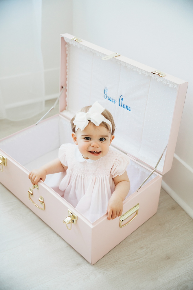 Grace smiling with her arms resting on the edge of an open pink trunk embroidered with her name at Reflection Images by Tracy Rowell in Florence SC