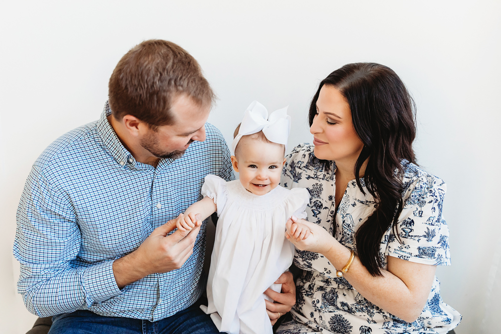 Elsie smiling between mom and dad, both holding her hands, family portrait in studio at Reflection Images by Tracy Rowell in Florence SC