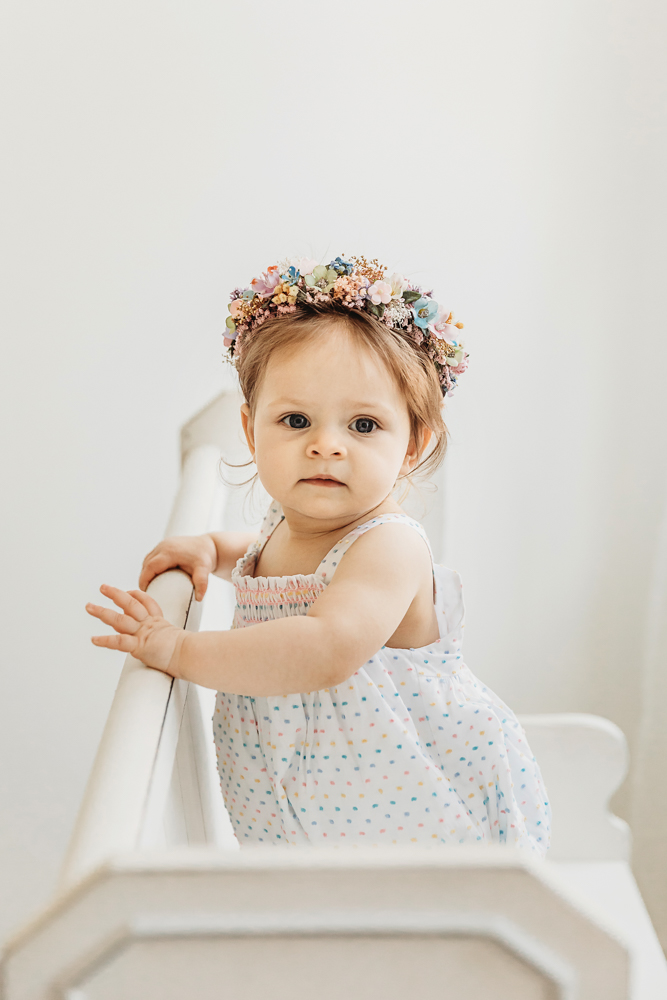 Livi Kate stands confidently holding a bench, wearing a colorful flower crown and birthday dress.