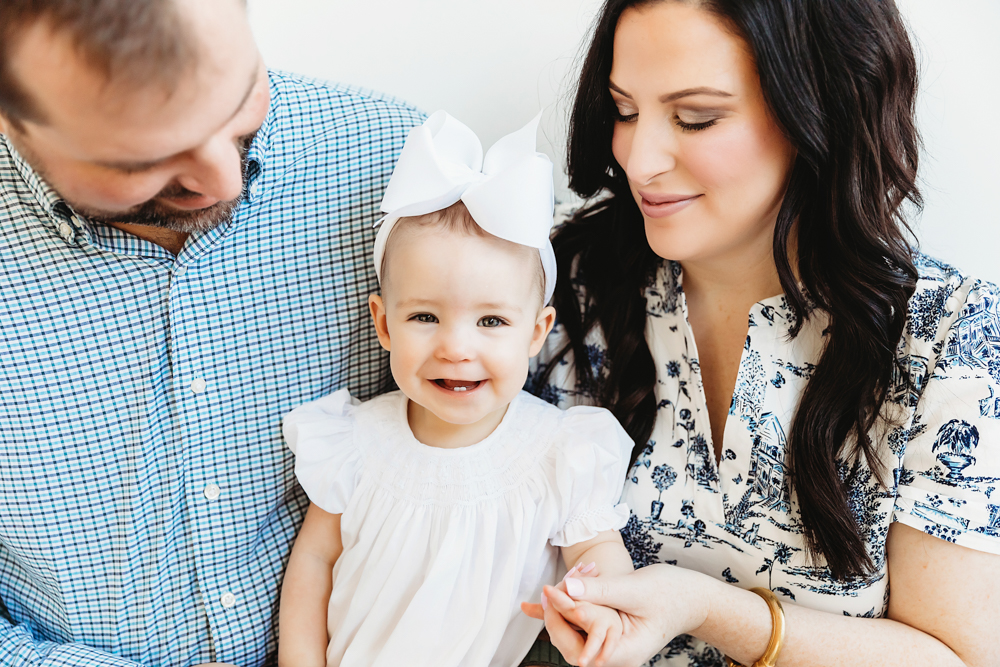 Close-up of Elsie smiling in white dress and bow, framed by mom and dad beside her at Reflection Images by Tracy Rowell in Florence SC