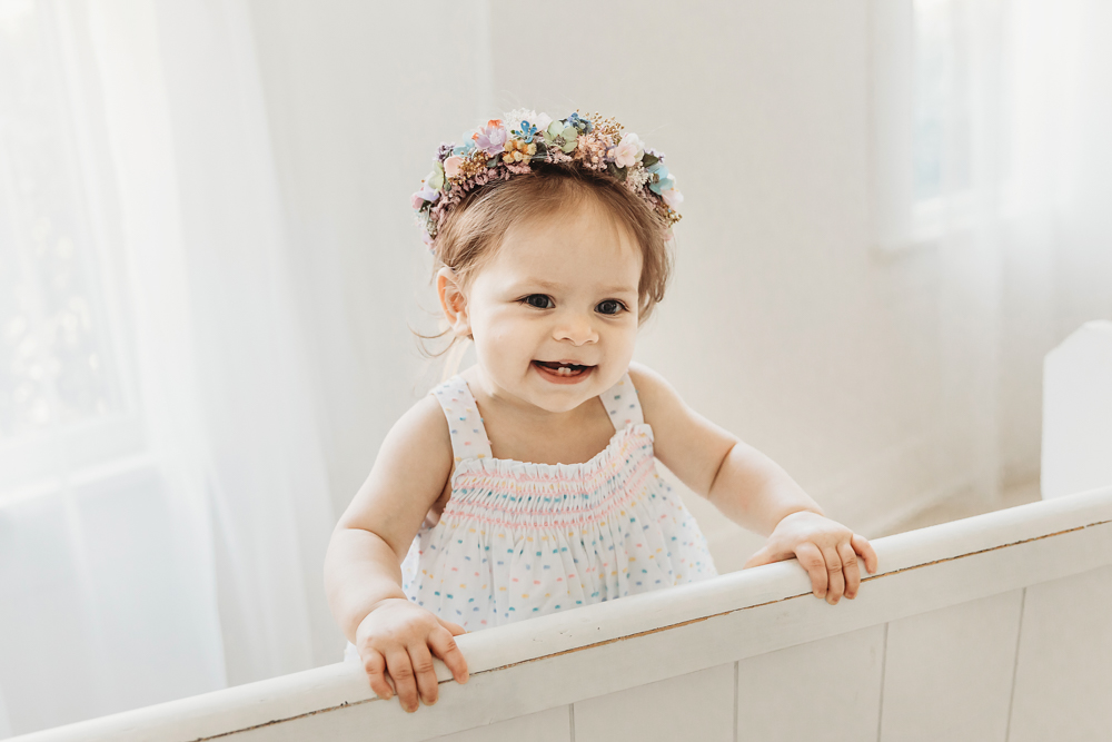 Livi Kate beams with joy while standing and holding the back of a white bench during her birthday shoot.