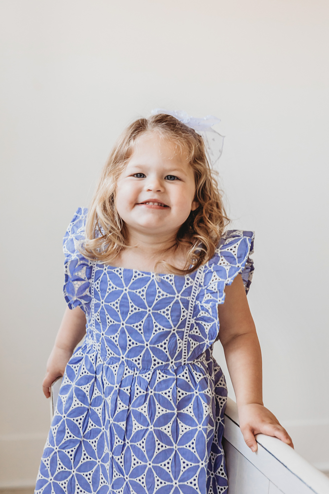 Livi Kates older sister smiles proudly in a lavender eyelet dress with a white bow in the studio.