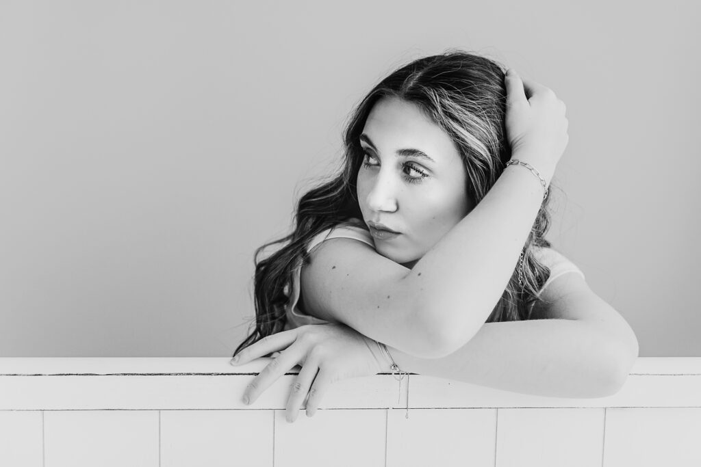 Black and white image of Addy posed at a white panel, looking off to the side with soft window light at Reflection Images by Tracy Rowell in Florence SC