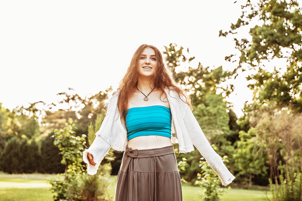Eve smiling with arms slightly outstretched, turquoise bandeau and cream sweater, bright sky and greenery at Reflection Images by Tracy Rowell in Florence SC