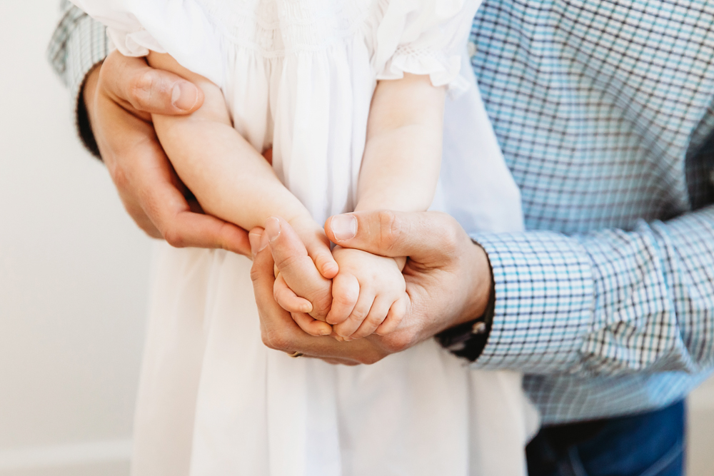 Close-up of Elsie’s tiny hands being held securely by dad, wearing white dress, milestone detail at Reflection Images by Tracy Rowell in Florence SC
