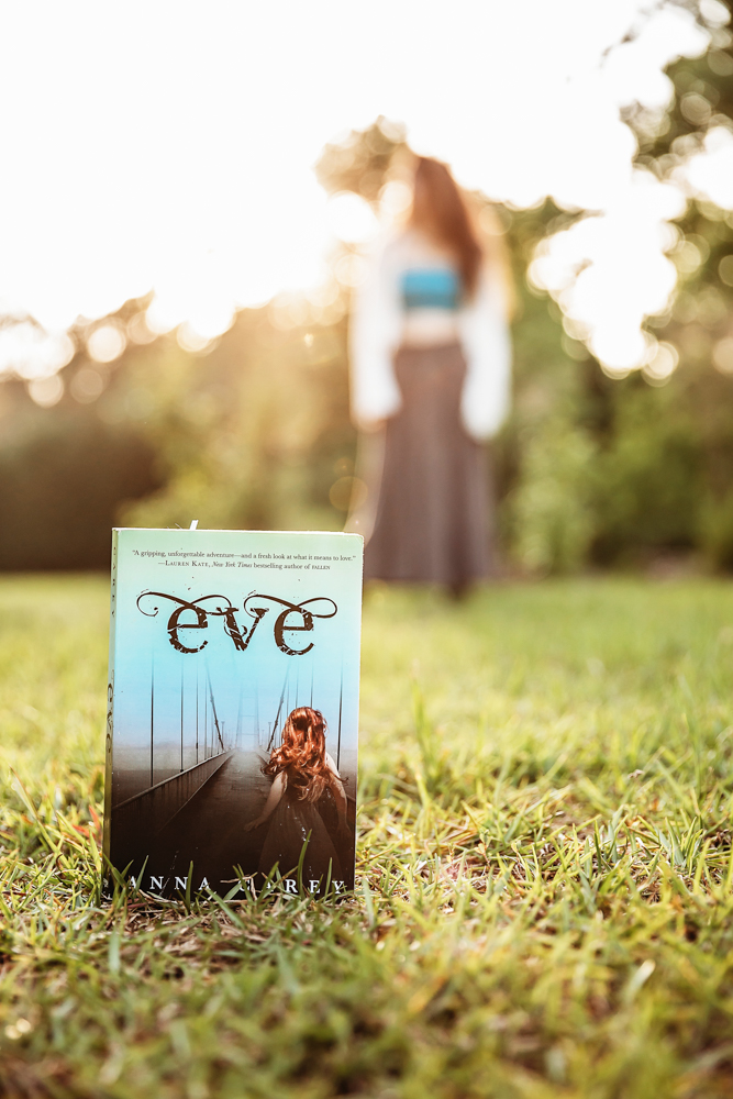 Close shot of book titled Eve placed on grass, blurred figure of Eve in turquoise top and long skirt in background at Reflection Images by Tracy Rowell in Florence SC