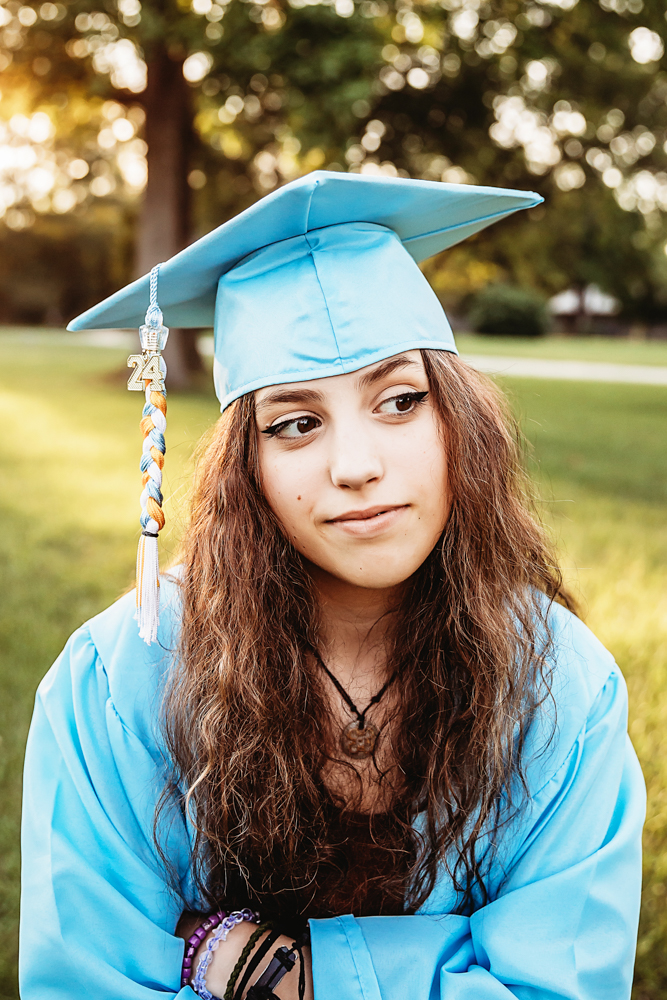 Close-up of Eve in light blue cap and gown, tassel 2024 visible, looking thoughtful in afternoon sunlight at Reflection Images by Tracy Rowell in Florence SC