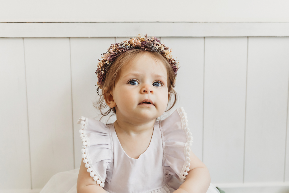 Close-up of baby girl in a white dress with flower crown and blue eyes during birthday photoshoot