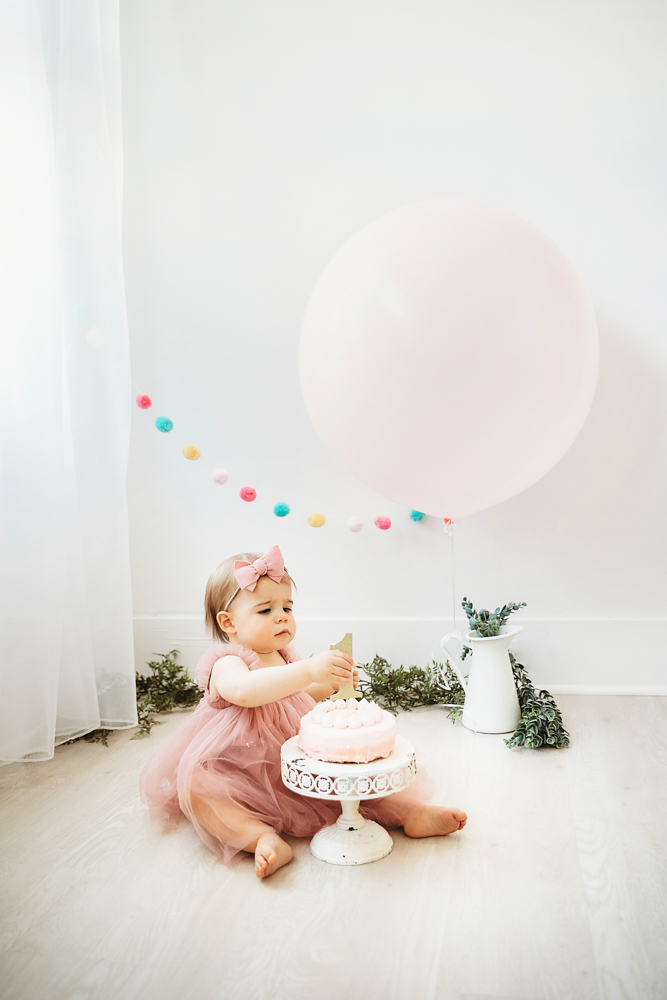 Grace starting her cake smash session in a mauve tutu dress with a large balloon and colorful felt garland backdrop at Reflection Images by Tracy Rowell in Florence SC