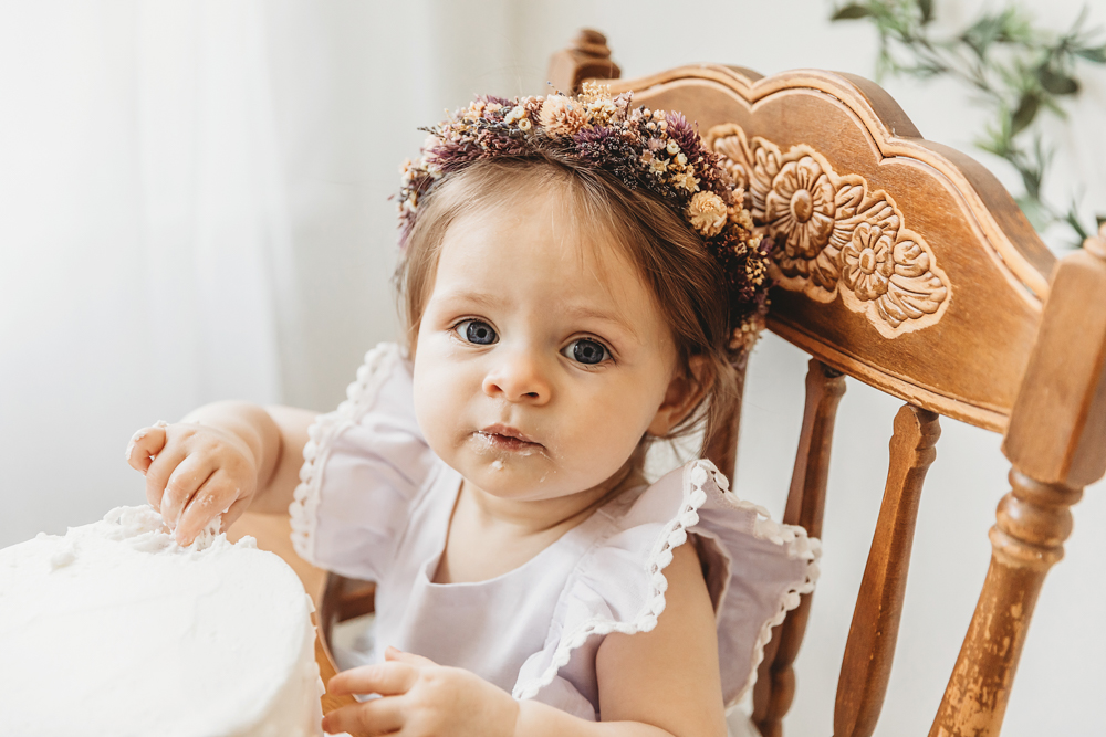 Close-up of birthday girl gazing curiously at the camera while sitting next to her cake